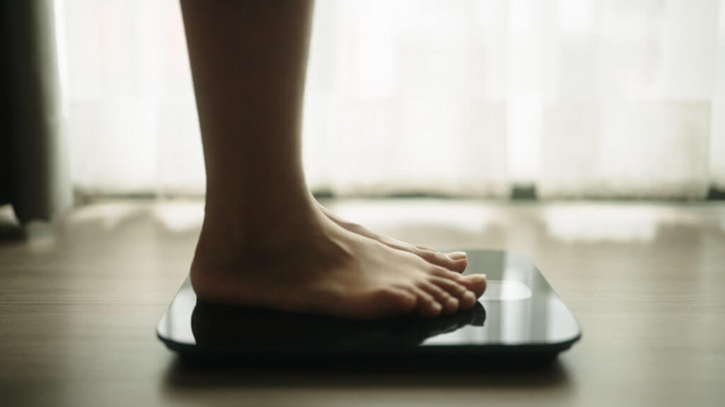 A person is standing on a body weighing scale to check for obesity.